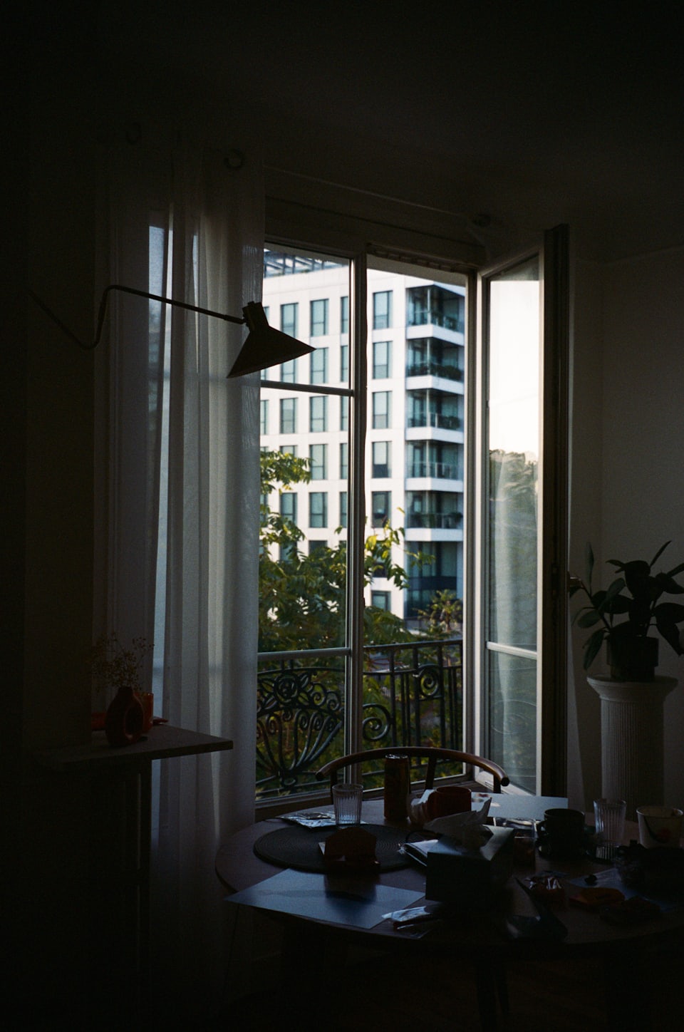 A lived-in room at dusk, a table by an open window looking onto the building opposite